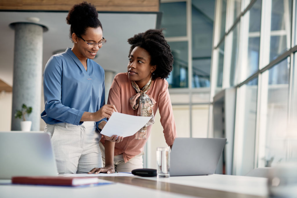 Black business mentor feeling satisfied with reports of her assistant who works at company office.